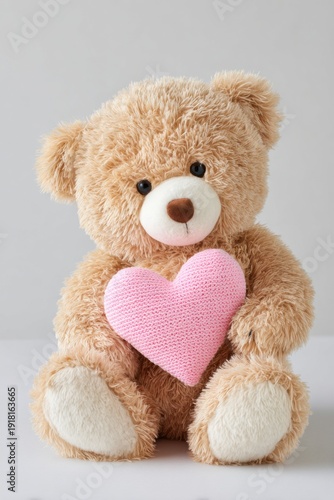 Fluffy handmade teddy bear holding a pink knitted heart, sitting on a light surface with a soft, neutral background, ideal for gifts and decorations