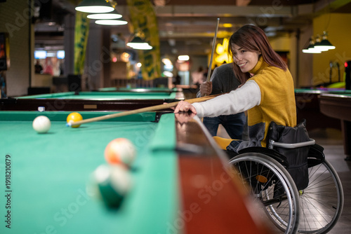 Young woman who uses a wheelchair and who is paralyzed playing billiards