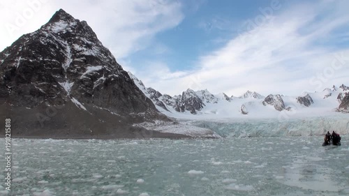 Journey through arctic scenery of Svalbard, Norway, amidst glacial ice. Behold towering mountains, pristine snow, and calm waters as small boat navigates icy terrain near majestic glacier.