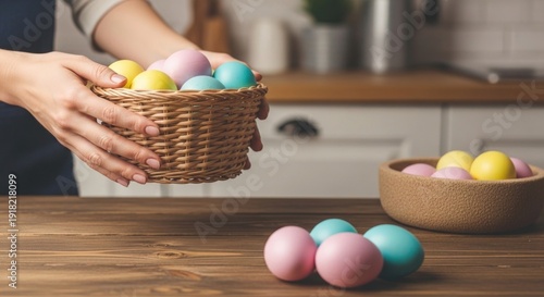 A person carries a woven basket full of pastel colored Easter eggs over a wooden kitchen counter beside a bowl of additional eggs.