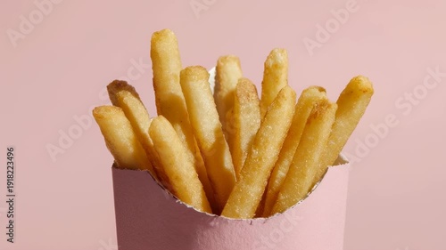 A close-up shot of golden french fries in a pink container against a soft pink backdrop