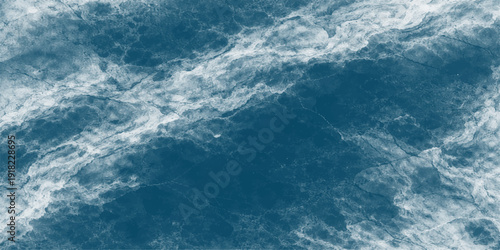 A bright summer sun shines through fluffy white clouds in a clear blue sky, reflecting light onto a beautiful abstract blue water surface with gentle waves for a calm nature background