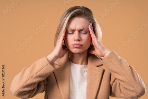 Woman touching temples, suffering from headache, blood pressure on beige. Pain.