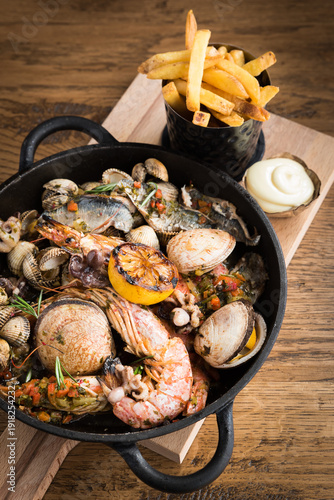 Foto A seafood stew in a pan on a wooden plank with fries and mayonnaise on a wooden