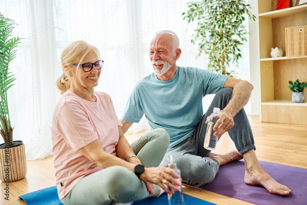 Obraz premium Portrait of a senior couple holding water bottle and exercise mat smiling and talking at home healthy living