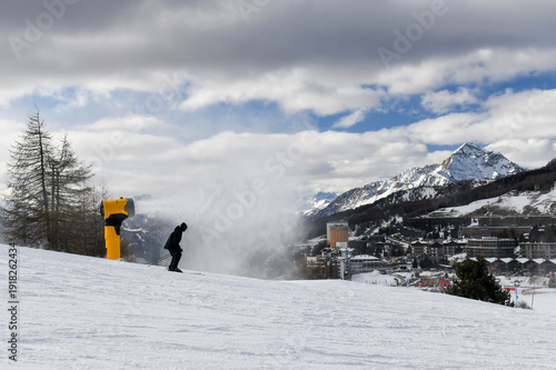 Skiers and snowboarders descending a ski slope in an Italian ski resort. People skiing down a wide snowy piste overlooking Sestriere town in the Piedmont region. Winter holiday resort in the mountains