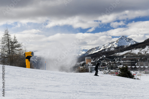 Skiers and snowboarders descending a ski slope in an Italian ski resort. People skiing down a wide snowy piste overlooking Sestriere town in the Piedmont region. Winter holiday resort in the mountains