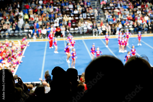 defocused Cheerleading event with teams performing in front of a large crowd at an indoor arena during a competitive match