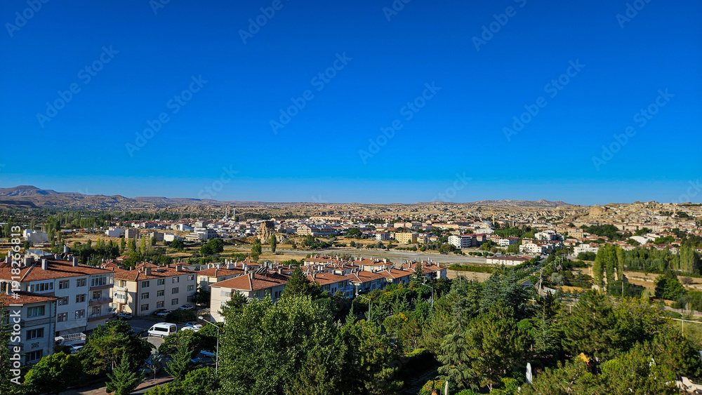 Obraz premium Suburban Town Under Clear Blue Sky, Tree Canopy And Mixed Rooftops, Grid Of Streets, Parks And Residential Blocks Stretching Toward Distant Hills.