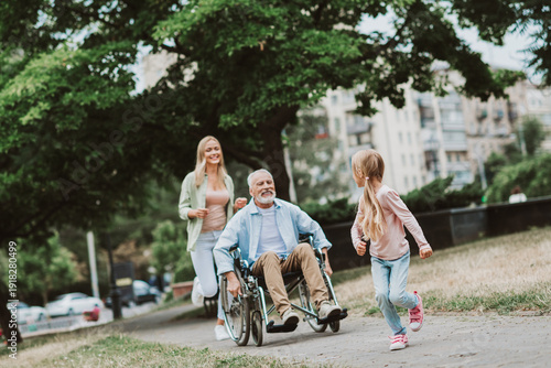 Fotografia Playful park scene with grandpa in a wheelchair joined by his daughter and grand