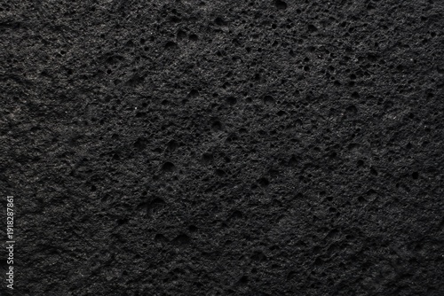 Black volcanic basalt rock surface with dense porous cavity texture