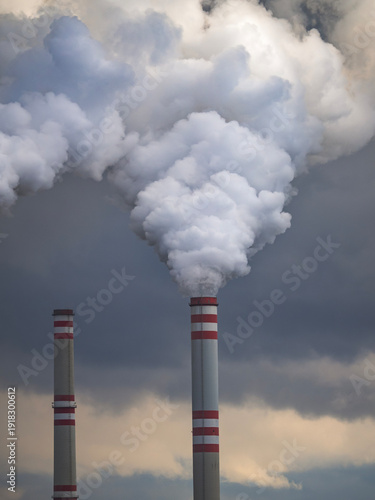 Tall industrial chimneys with red and white stripes emitting thick smoke into dark dramatic sky
