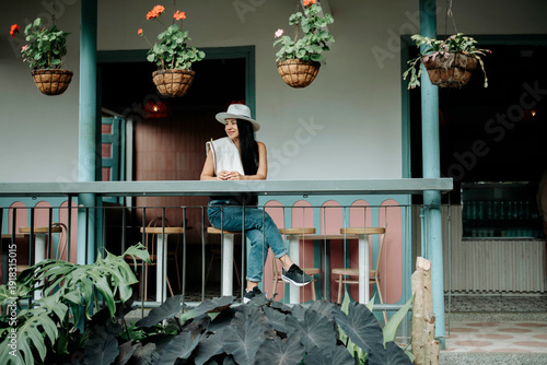 Bild auf Leinwand Woman sitting on colonial balcony surrounded by hanging plants