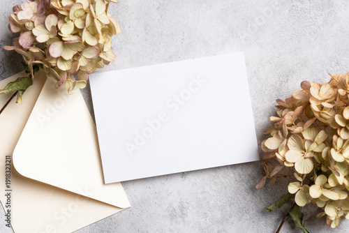 Blank invitation or greeting card mockup with an envelope and dried hydrangea flowers arranged on a textured gray surface for design purposes