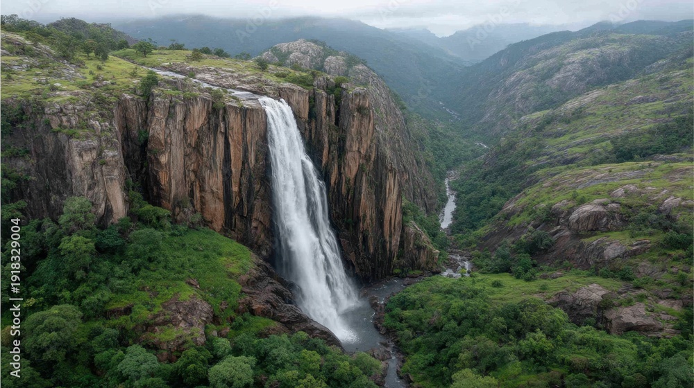 Obraz premium Majestic Waterfall Cascading Down Rocky Cliffs Surrounded by Lush Greenery Under Overcast Sky in a Serene Natural Landscape