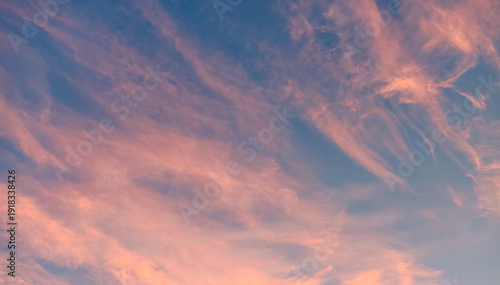 Soft pink and orange clouds glowing at sunset against a blue evening sky. Dreamy pastel atmosphere with delicate cloud formations and tranquil mood