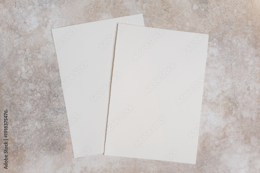 Fototapeta premium Two sheets of deckle edge cotton watercolor paper placed on a textured surface, showcasing the natural fibers and unique edges of the paper