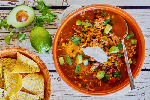 taco soup with shredded chicken, cheddar cheese, avocado, fresh cilantro and lime juice