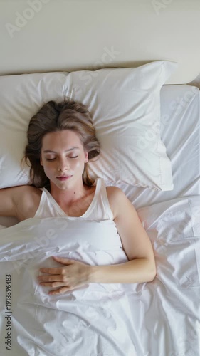 A serene young adult woman with light brown hair sleeps soundly in a cozy bed adorned with clean white linens, showcasing a peaceful moment of rest and relaxation.