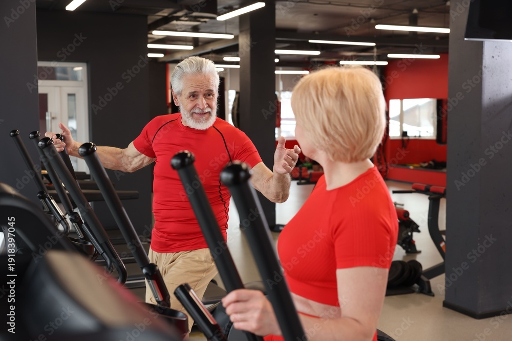 Fototapeta premium Senior couple training on elliptical machines in gym