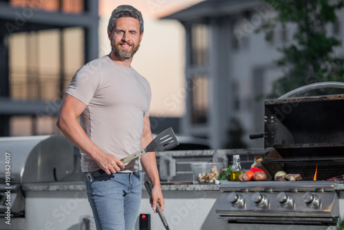 Handsome man preparing barbecue. Male cook cooking meat on barbecue grill. Guy cooking meat on barbecue for summer family dinner at the backyard of the house.