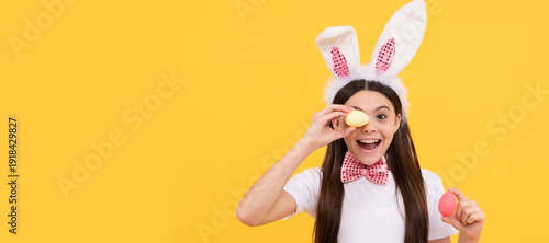 surprised easter teen girl in bunny ears and bow tie hold painted eggs. Easter child horizontal poster. Web banner header of bunny kid, copy space.