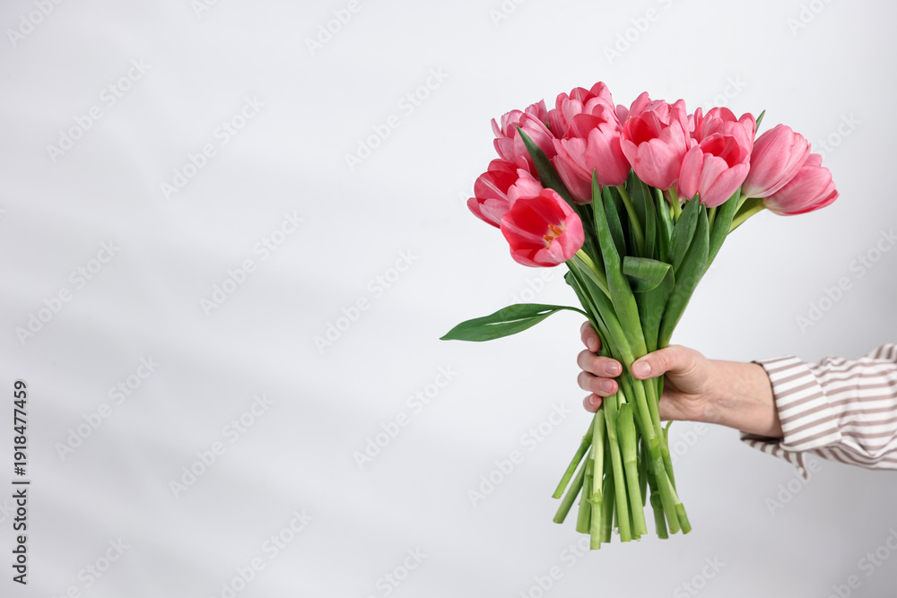 Naklejka premium Woman with bouquet of pink tulip flowers near light grey wall, closeup. Space for text