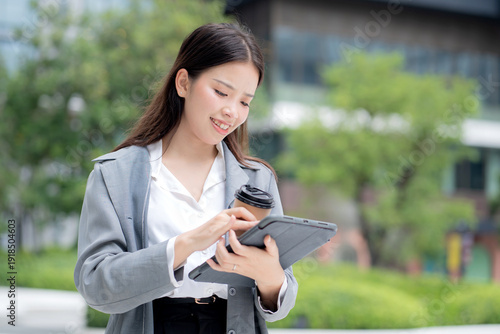 Wallpaper Mural Happy young asian businesswoman standing holding coffee while using tablet outdoors city, digital nomad, business woman or manager touching tablet for working, modern technology, digital device. Torontodigital.ca