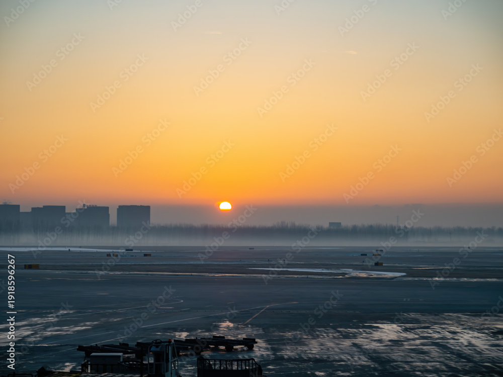 Naklejka premium Sunset glows over frozen airport tarmac at dawn.
