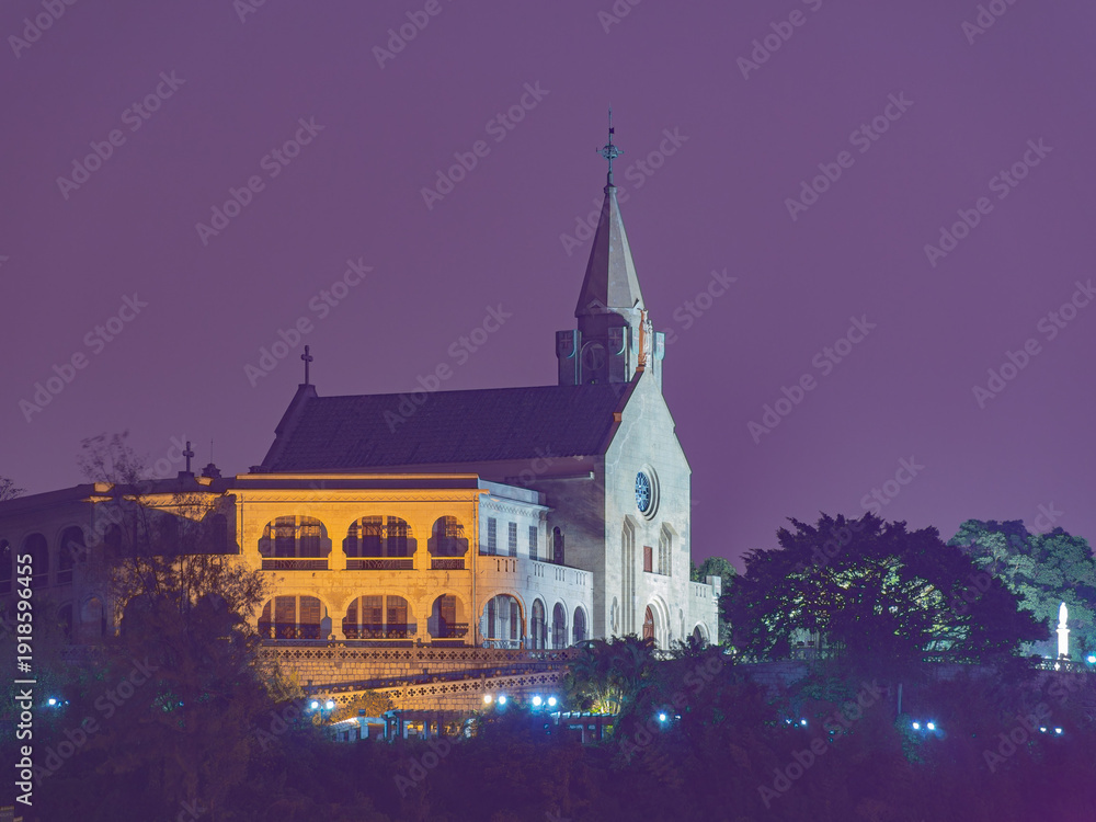 Obraz premium Illuminated church with spire stands against purple night sky.