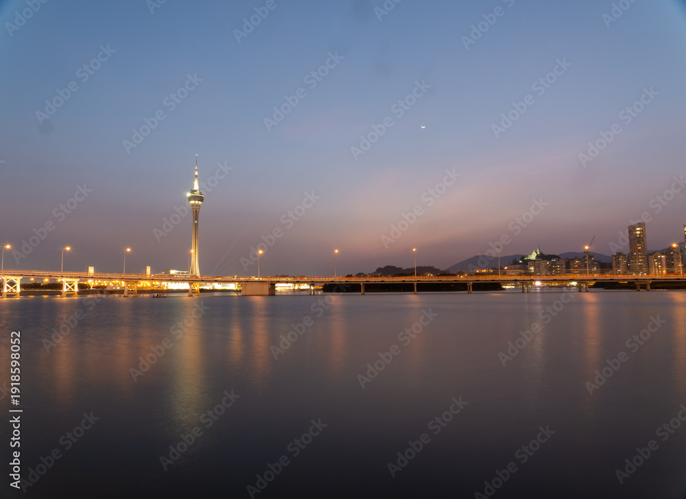 Fototapeta premium Macau tower illuminated at twilight over calm waters.