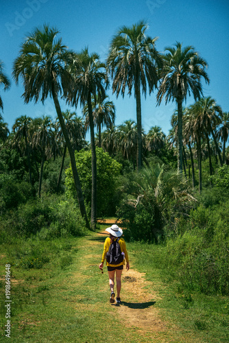 A girl wearing a hat and a yellow shirt is walking on a path in El Palmar National Park
