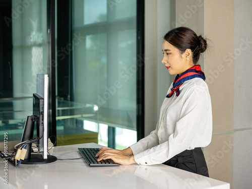 Wallpaper Mural Professional air hostess working at desktop computer in check-in counter, typing on keyboard, corporate administration, customer service, workplace productivity concept Torontodigital.ca