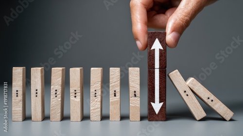 Human hand strategically places a stabilizing wooden block with bidirectional arrows amid toppling pieces