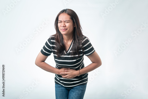фотографія A young Indonesian woman grimacing in pain while clutching her stomach