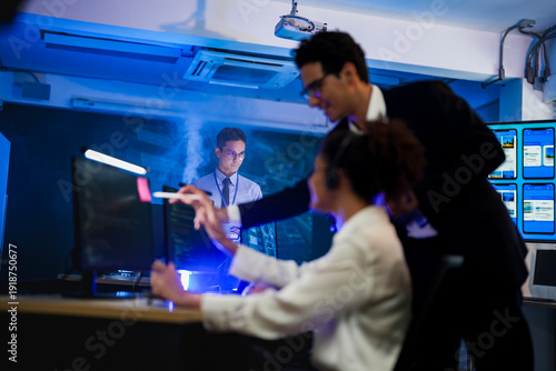 Friendly female IT support agent wearing headset working on computer in dark blue office. Professional customer service operator helping client in night shift control center room.