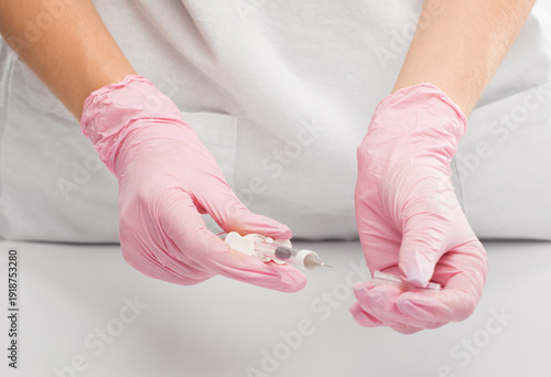 A cosmetologist in a white coat holds an injection syringe in his hands.