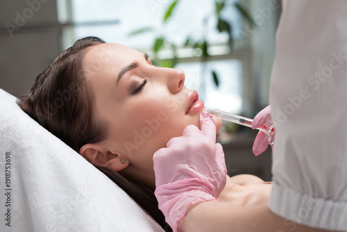 Cosmetologist does injections for lips augmentation and anti wrinkle in the nasolabial folds of a beautiful woman. Women's cosmetology in the beauty salon.