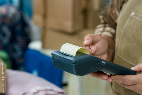 Bild auf Leinwand Senior asian retired businesswoman holds POS terminal, prints receipt, checks paperwork order processing, verifies transaction total, prepares parcel packaging for small business online shipping