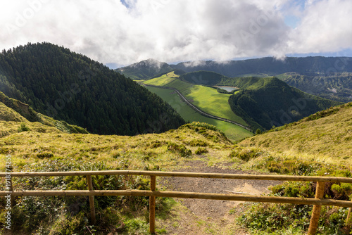A lush green hillside with a wooden fence and a view of a lake at Sete Cidades, Azores