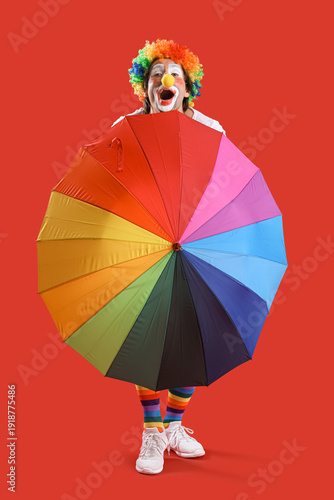 Portrait of clown with colorful umbrella on red background. April Fool's day ...
