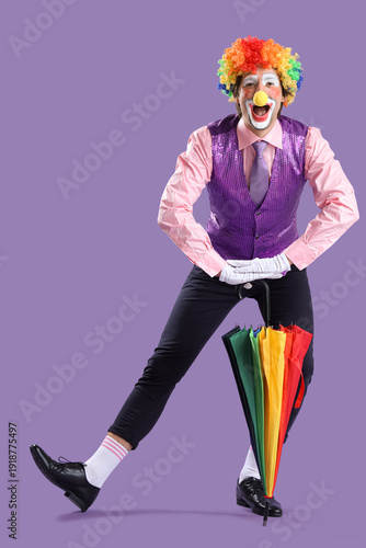 Portrait of clown with umbrella on lilac background. April Fool's day celebra...