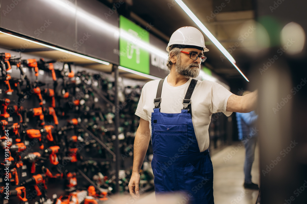 Fototapeta premium Worker in safety helmet browsing power tools in hardware store