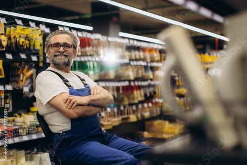Obraz na plátně Experienced hardware store worker sitting, smiling in aisle