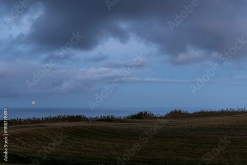 A cloudy sky with a red full moon in the background above the sea.
