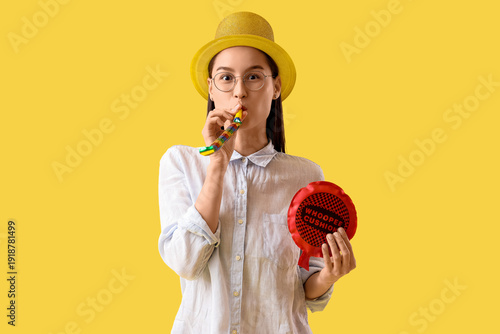 Businesswoman with party blower and whoopee cushion on yellow background. Apr...