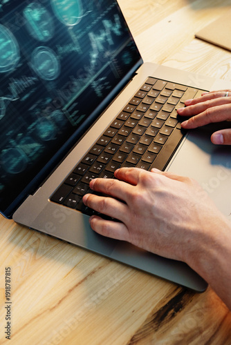 Hands typing on a laptop showing data and graphs in a workspace during daytime