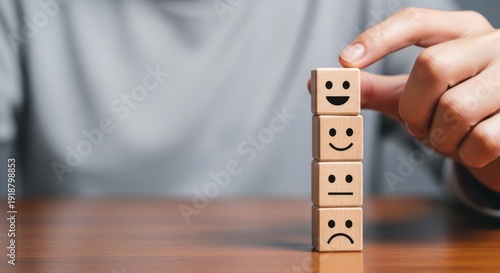 A person selects a smiley face from a stack of wooden blocks with various facial expressions on a wooden table