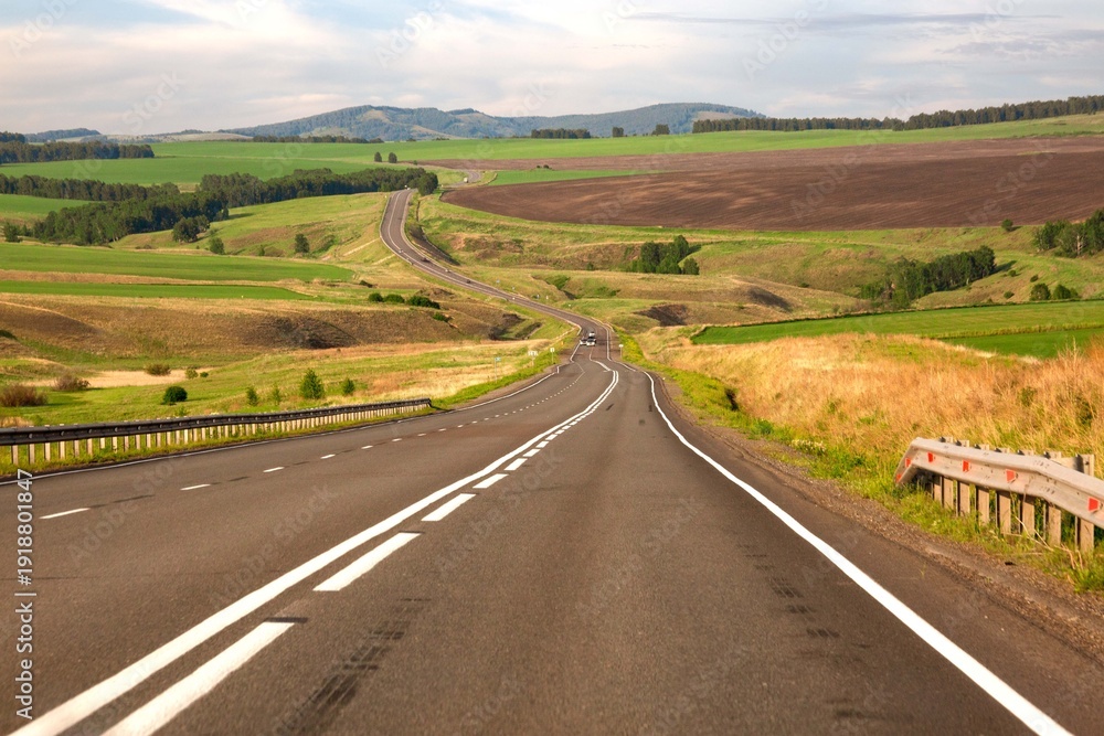 Obraz premium Asphalt country road among fields and picturesque nature