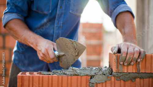 Bricklayer Installing Red Clay Bricks with Trowel and Cement Mortar on Construction Site